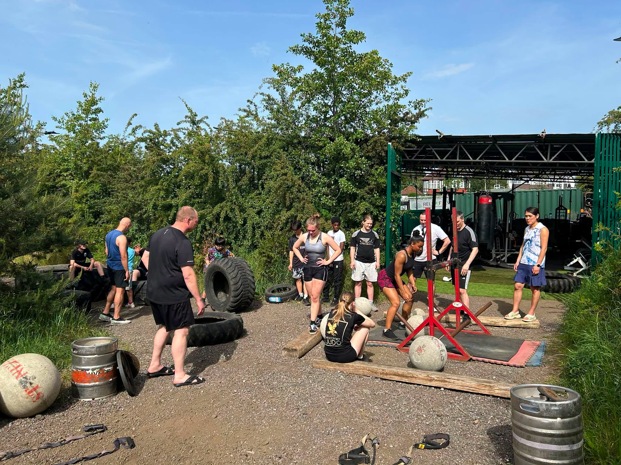 a group of 5 people exercising outside with atlas balls and tractor tyres