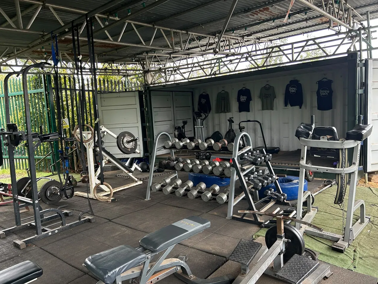 rack of free weights, bench and pull up bar with merch hanging in the background